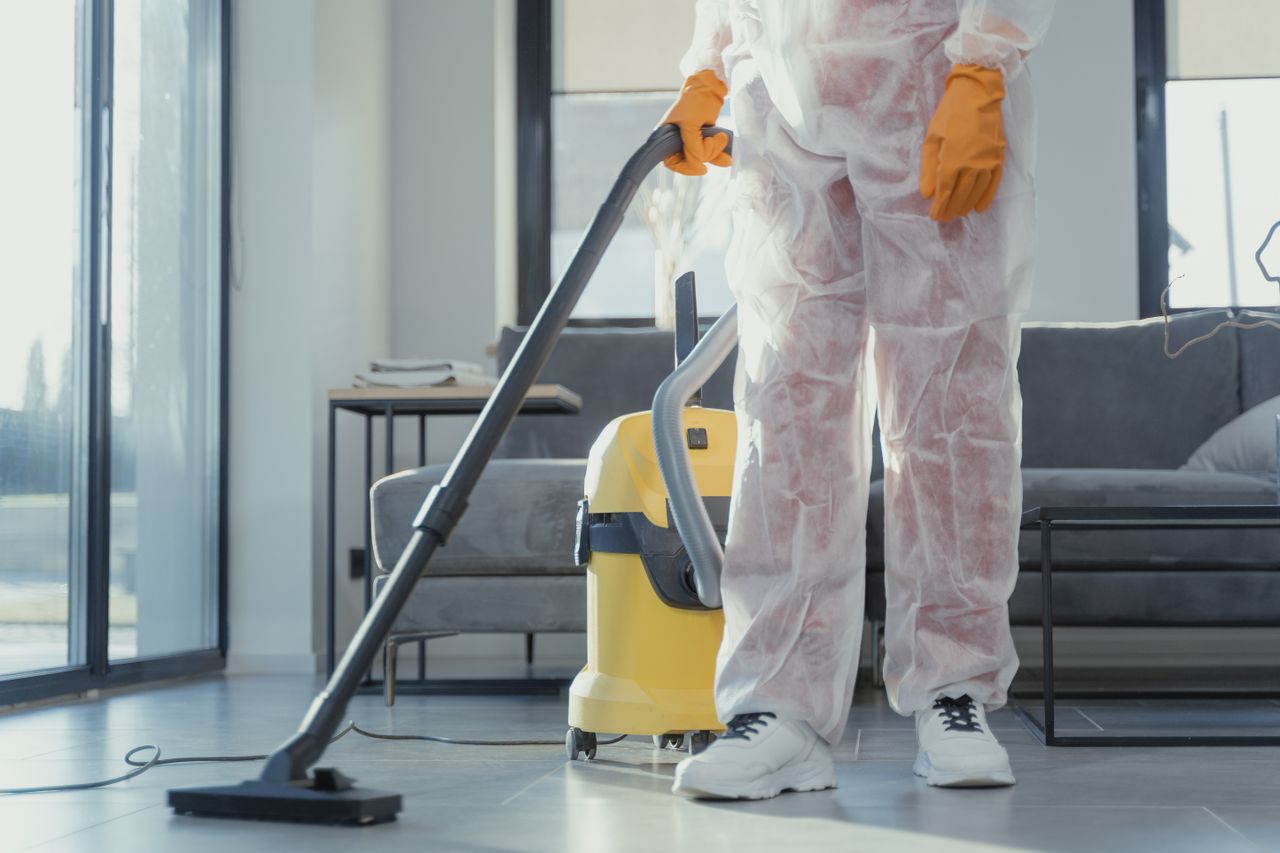 about-02 A cleaner in protective coveralls and gloves vacuuming a modern living room.