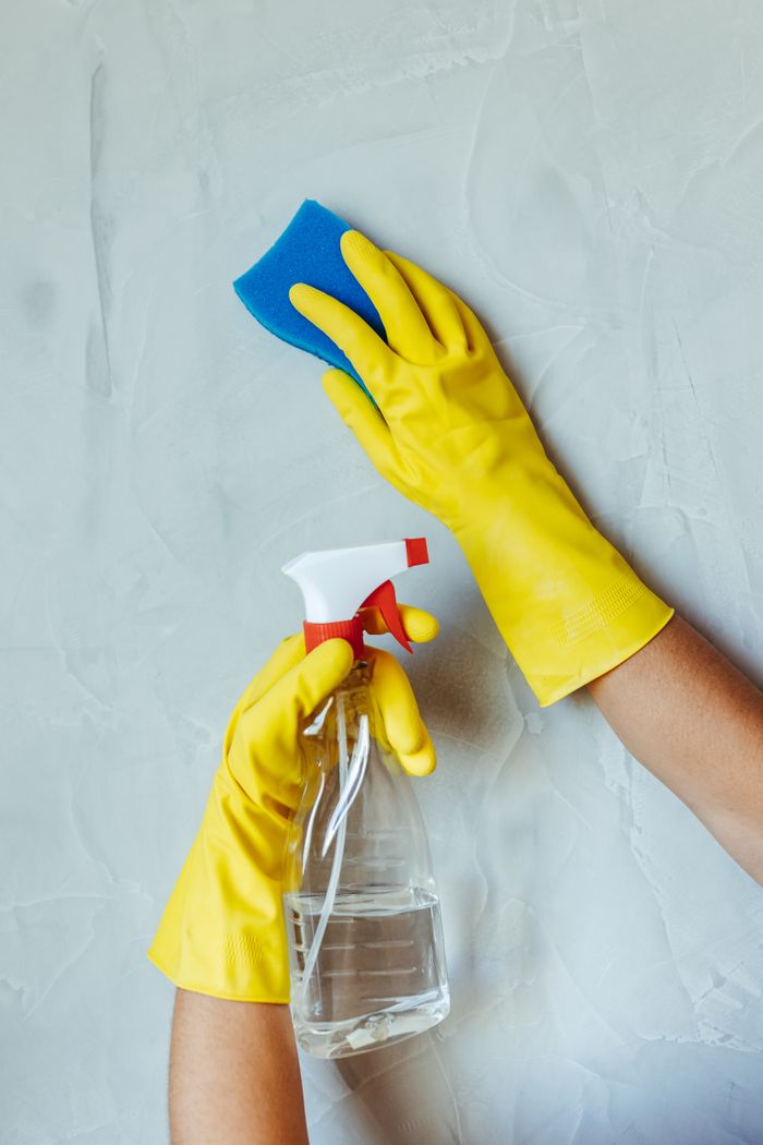 hero-img-01 Hands in yellow gloves cleaning wall with sponge and spray bottle.
