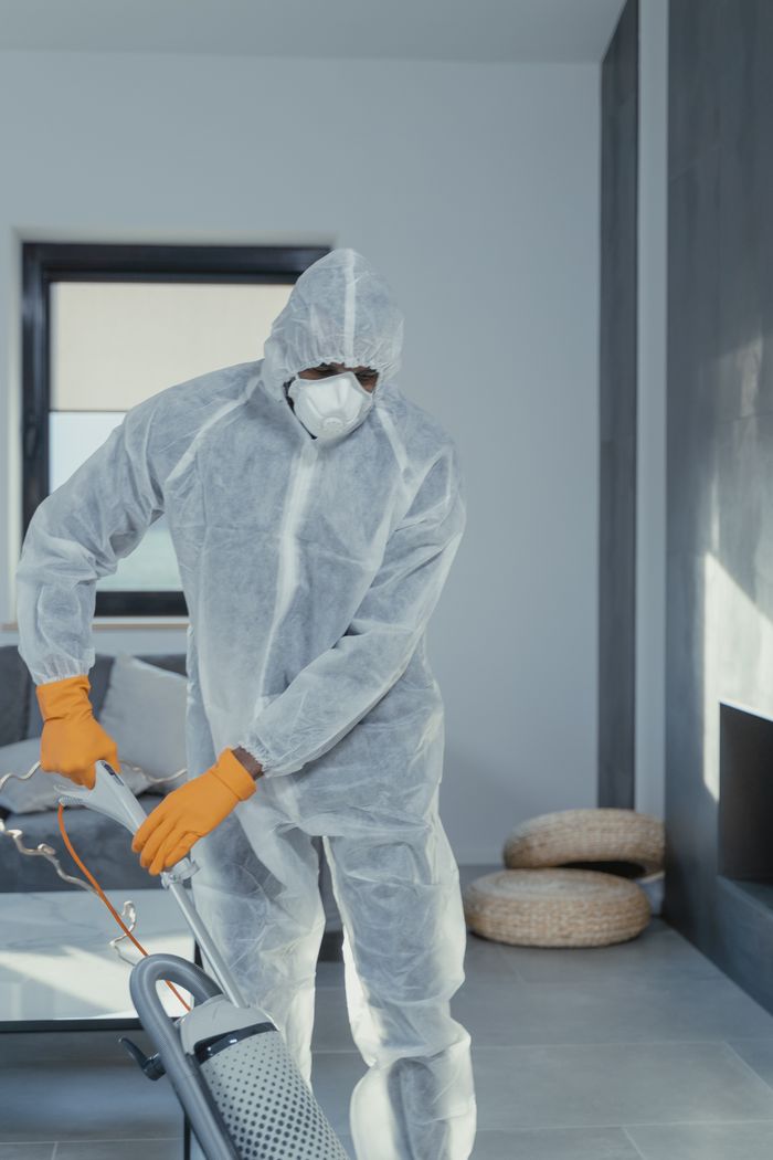 about-01 A person in personal protective equipment vacuuming indoors, ensuring a thorough clean.